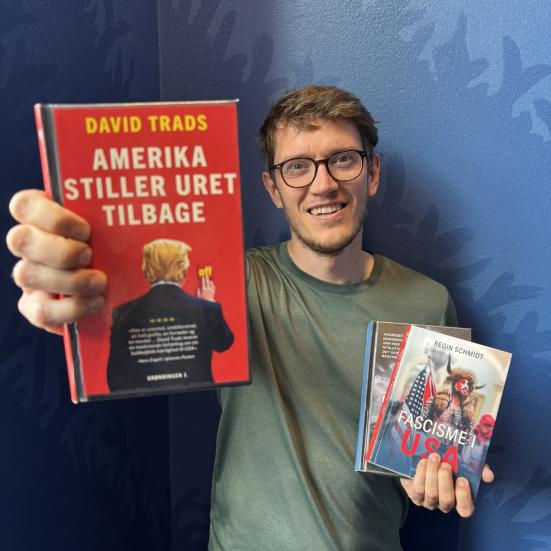 Billedet viser kulturformidler Dennis Odgaard med tre bøger, hvor den ene bog holdes frem mod kammeraet. Bøgerne handlet om USA.