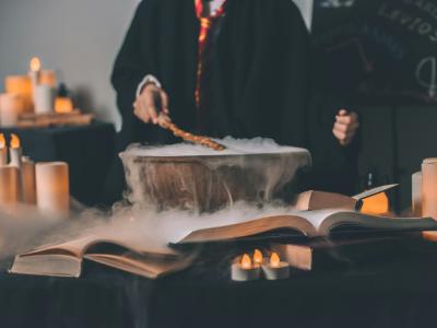 person står med tryllestav over rygende gryde