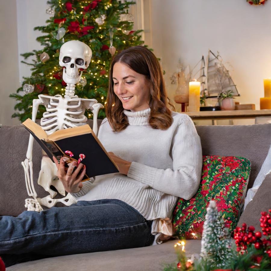 AI-genereret billede. En ung kvinde og et skelet sidder og læser en bog i julepyntet stue.